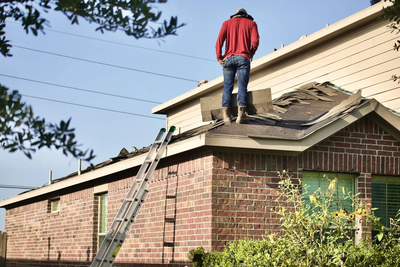 A roofer tearing off old shingles on a house roof