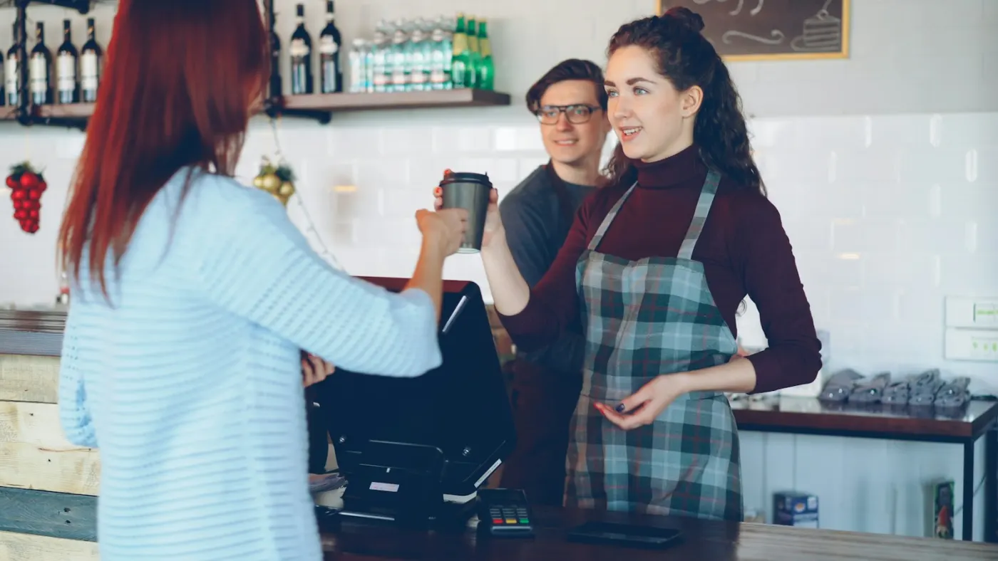 A barista handing a takeaway coffee to a customer across the counter